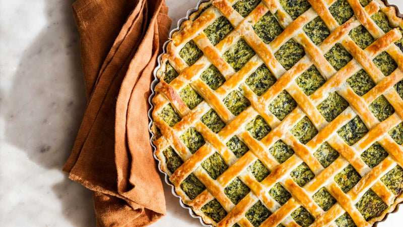 A ricotta and broccoli rabe tart with a golden lattice crust, the bright green filling visible through the weave.