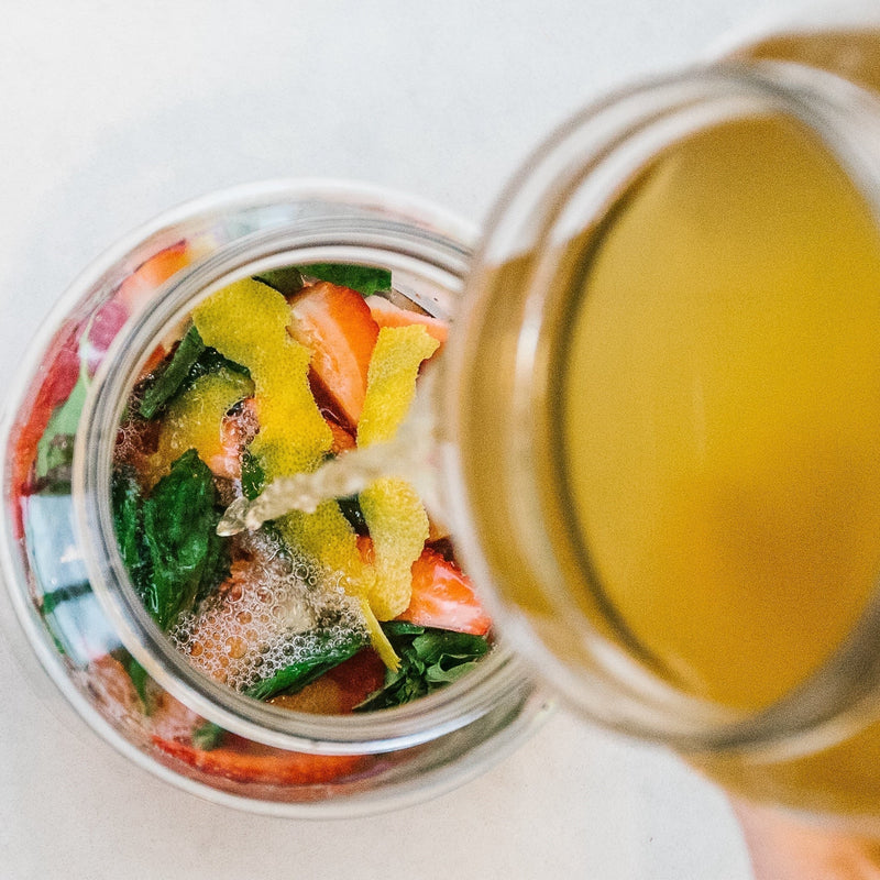 Pouring kombucha into a jar of strawberries, basil and lemon peel