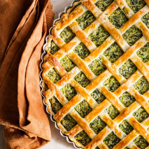 A ricotta and broccoli rabe tart with a golden lattice crust, the bright green filling visible through the weave.