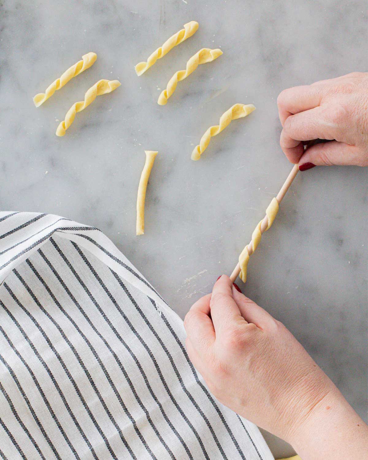 Hands rolling fresh semolina pasta twists beside a striped kitchen towel