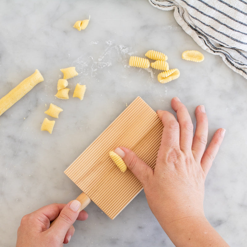 Hands shaping cavatelli pasta on a ridged gnocchi board