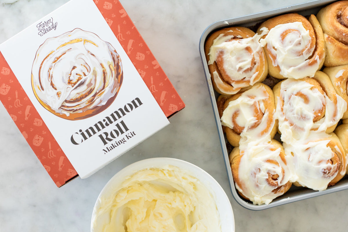 Frosted cinnamon rolls in the pan beside the FarmSteady Cinnamon Roll Making Kit