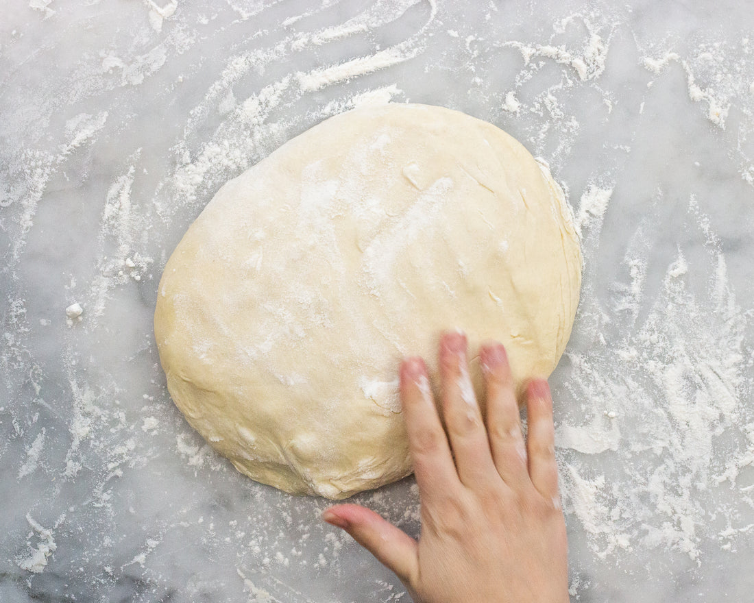 hand pressing flattened pizza dough round on marble