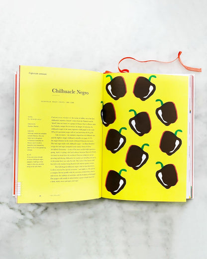 An Anarchy of Chillies book by Caz Hildebrand opened to a page on Chilhuacle Negro peppers, laying on marble.
